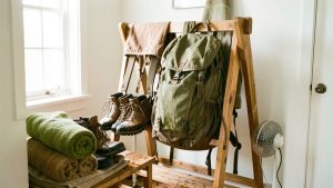 Chaussures de randonnée mouillées et sac à dos ouverts sur un support en bois dans une pièce aérée et lumineuse, avec une petite ventilation pour les sécher.
